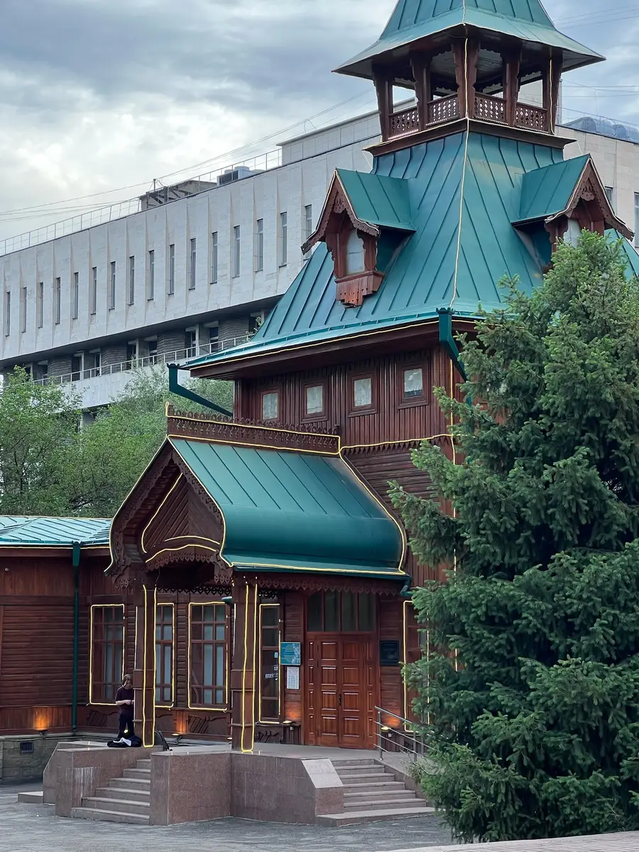 Historic wooden Almaty building with a green tiered roof and tower, gilded trim on its entrance